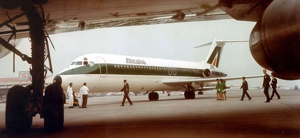 Alitalia airplane on runway with crew and ground staff walking nearby under the wing.