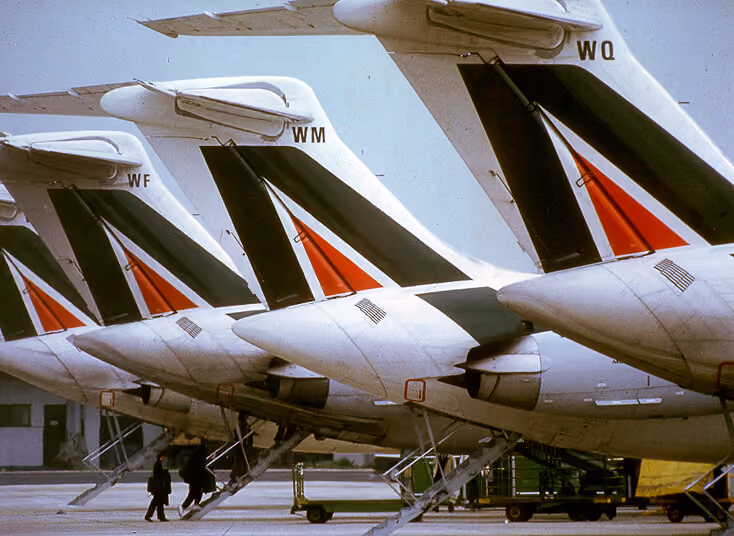 Row of aircraft tails with black and red stripes and different two-letter codes at an airport.