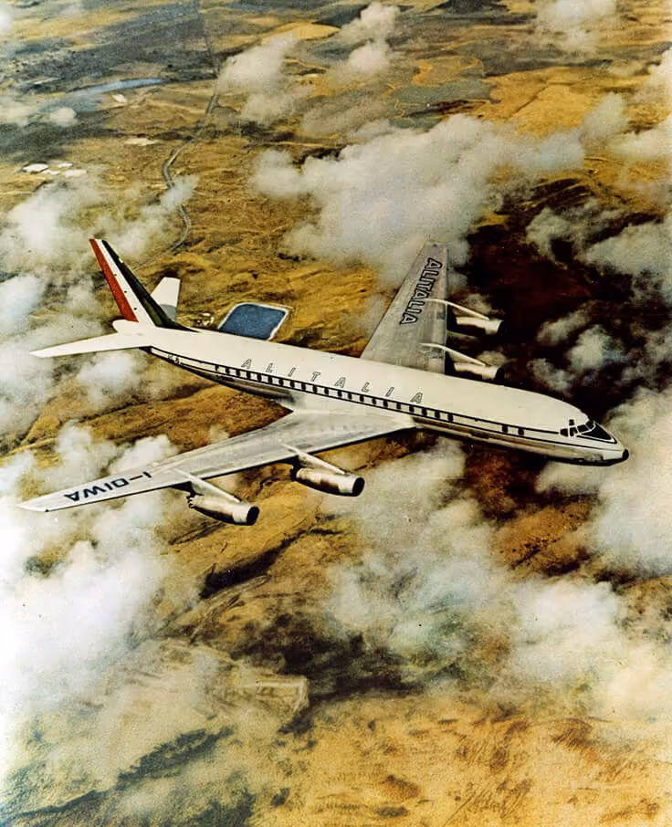 Alitalia passenger airplane flying above clouds over brown terrain.